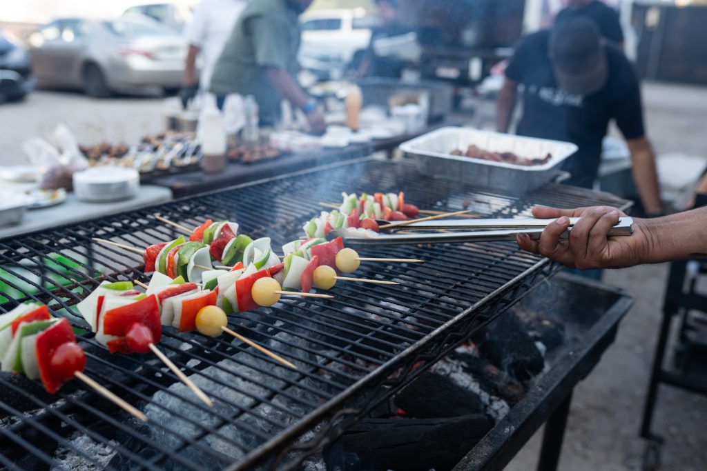 Vegetable skewers featuring peppers, tomatoes, and onions on a BBQ cooking away.
