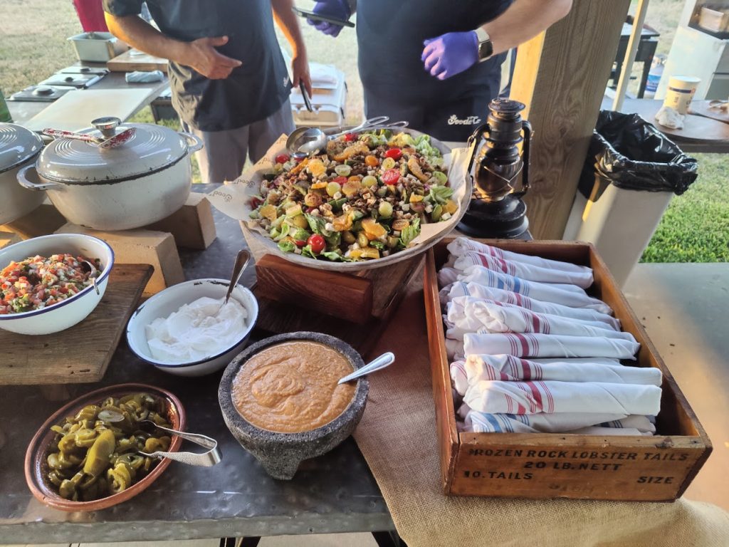 A food station featuring salads, rolled cutlery in napkins, jalapenos, pico de gallo, and sour cream.