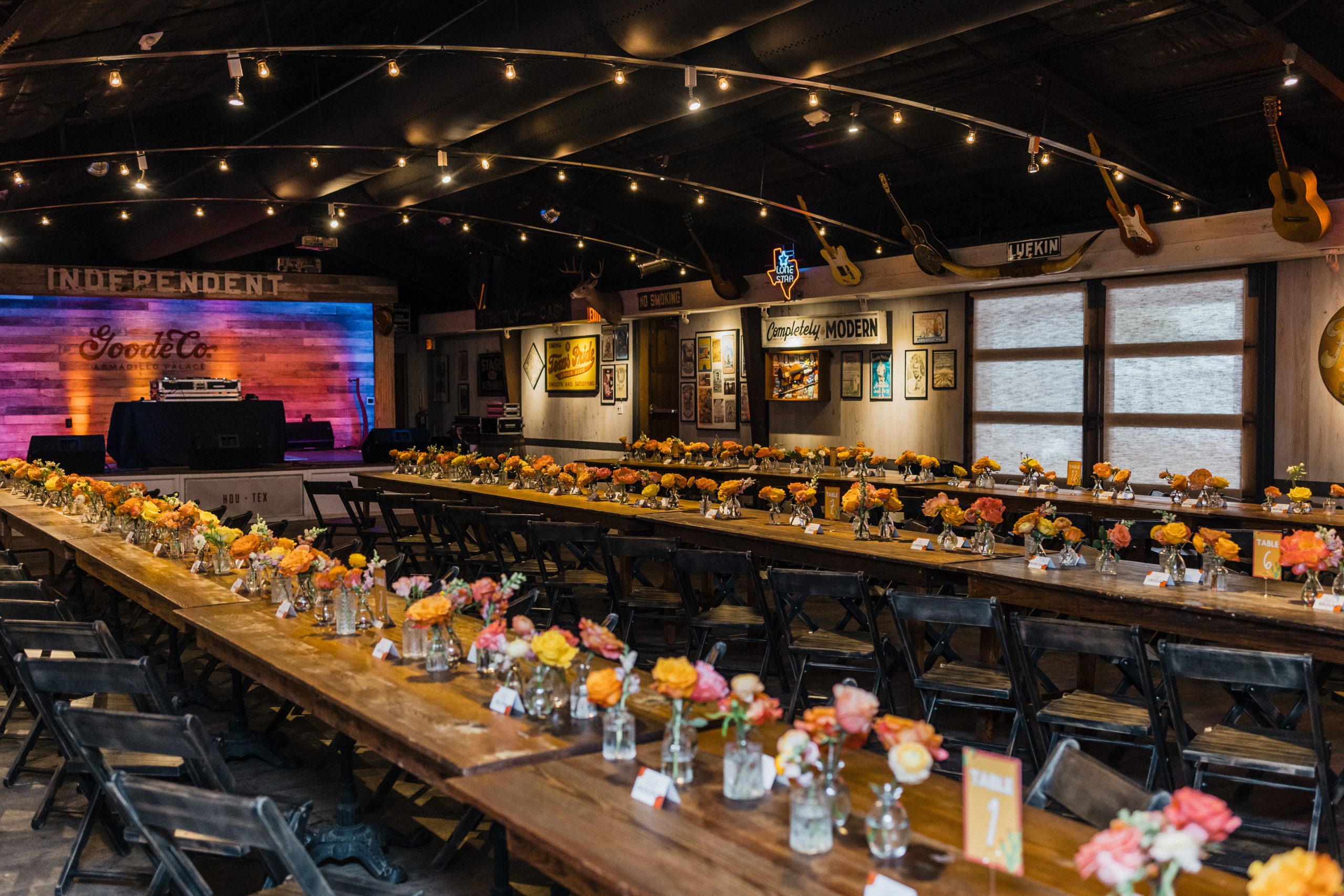 Wide shot of dining room with flowers, place cards, cutlery, and DJ at one end.
