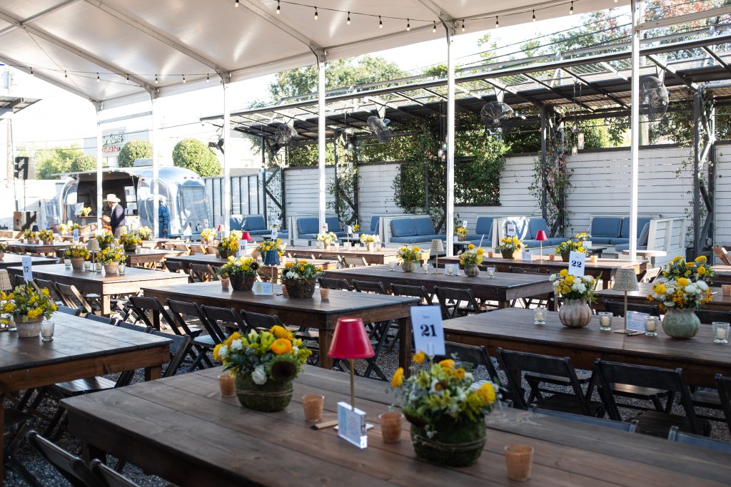 Rows of picnic tables with place settings, table numbers, and chairs all under a canopy.